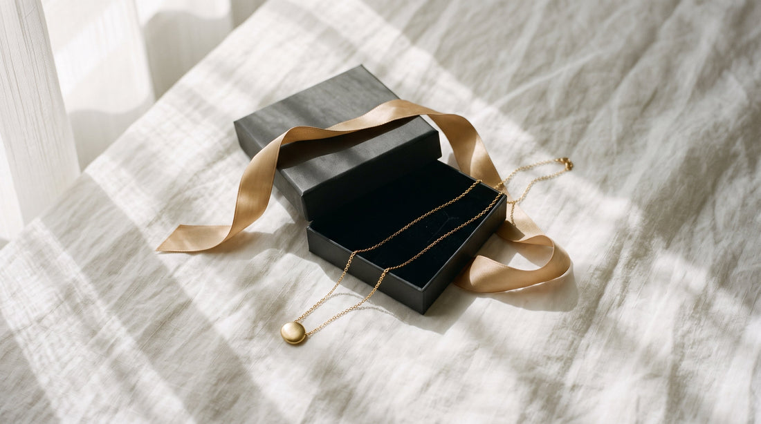 A gold necklace in a gift box with a gold ribbon